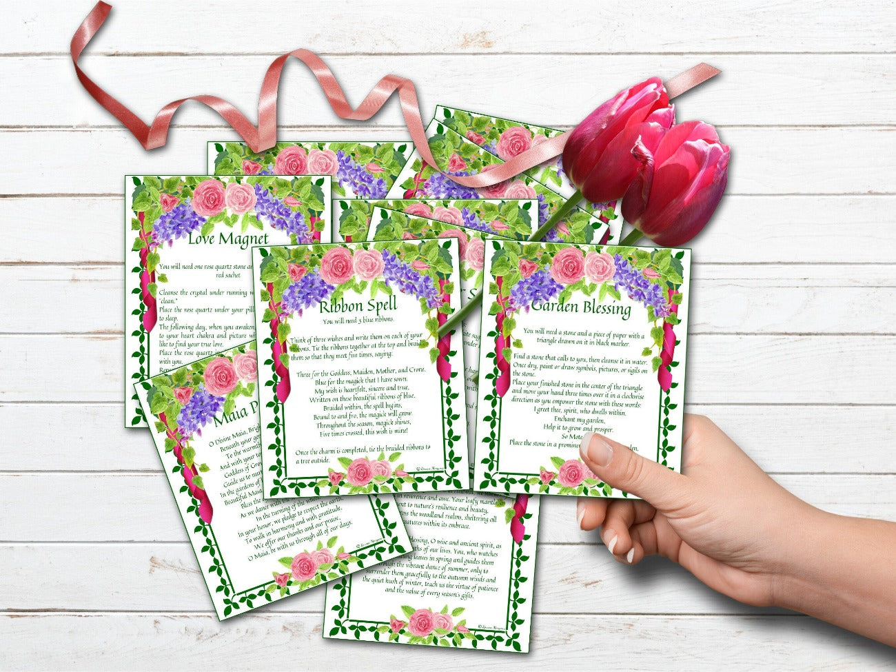 BELTANE SPELL CARDS, shown placed in a pile on a white wood background with a hand holding on of the cards - Morgana Magick Spell