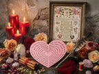 Decorative setup with candles, flowers, a heart-shaped paper, and a framed text on a stone wall background.