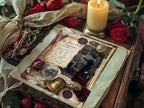 Moody product photo of a vintage-inspired gothic journal page with candle snuffer artwork, red roses, a lit pillar candle, black lace, wax seals, and layered antique parchment on a rustic wood surface.