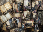 Artfully arranged flat lay of Victorian-inspired gothic journals and spellbooks on dark wood, surrounded by dried flowers, lace trim, old keys, handwritten papers, and witchy vintage décor.