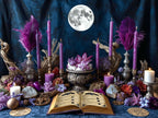 Magical moon altar with candles, books, and crystals against a dark blue background with a full moon.