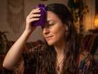Woman holding a purple charm bag against her forehead.
