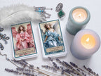 Two angelic tarot cards with candles, lavender, and jewelry on a white surface
