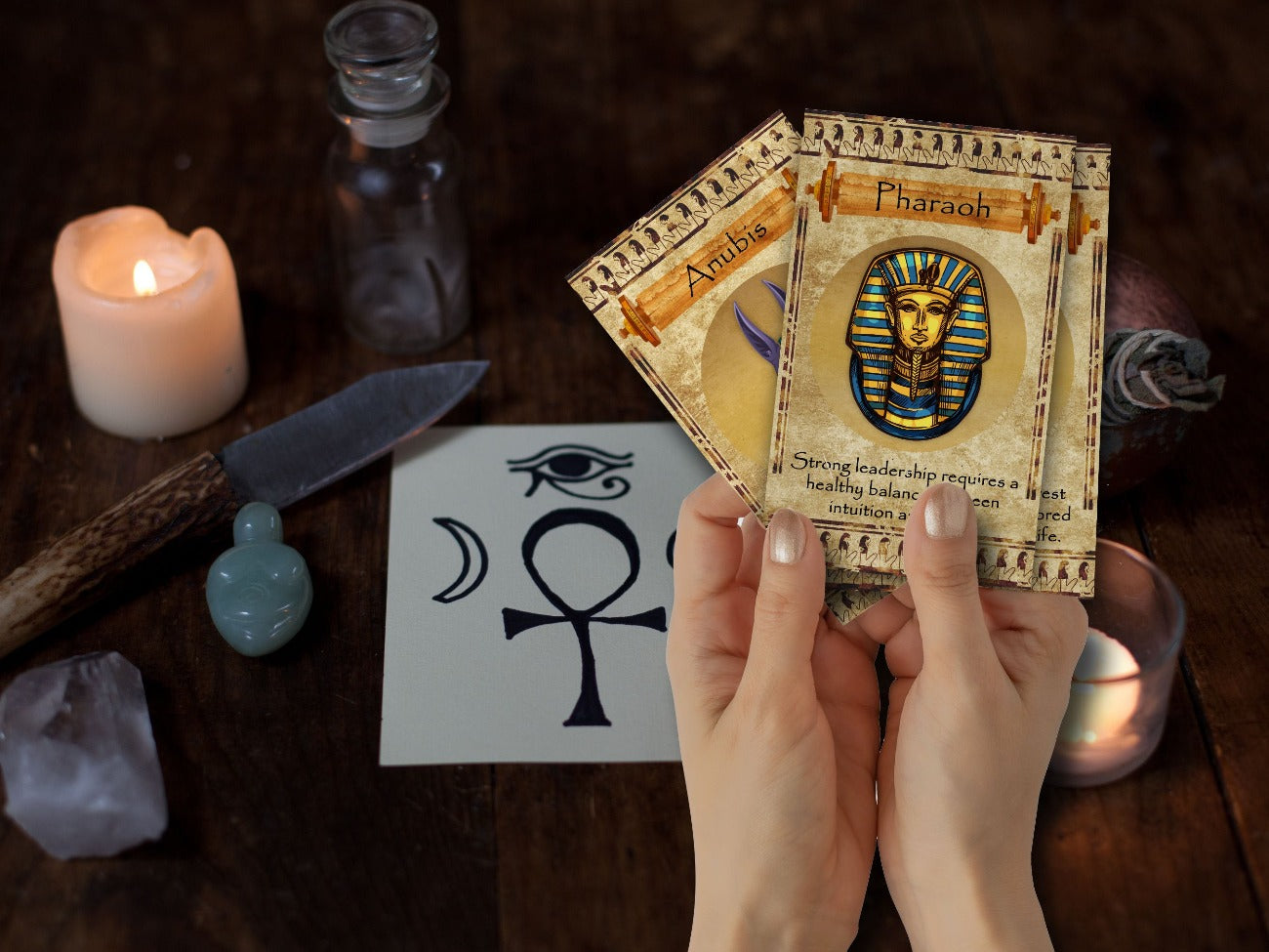 Image of hands holding three Egyptian Oracle cards in front of an Egyptian-inspired witch&#39;s altar.